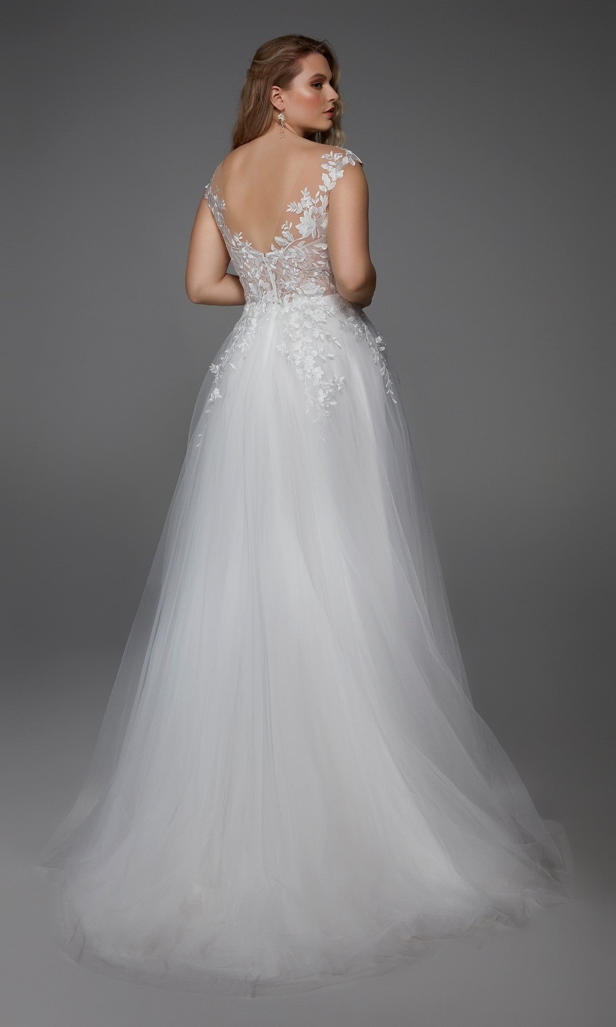 A woman in the Alyce 5090 long formal dress—sleeveless, white, with lace embroidery, sheer lace back, floral appliqué, and an elegant A-line tulle skirt—stands against a plain gray background.